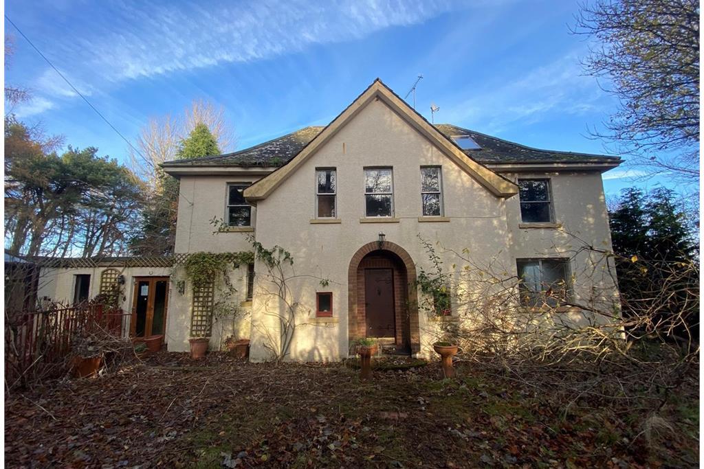 A large, white house with an overgrown garden and blue skies