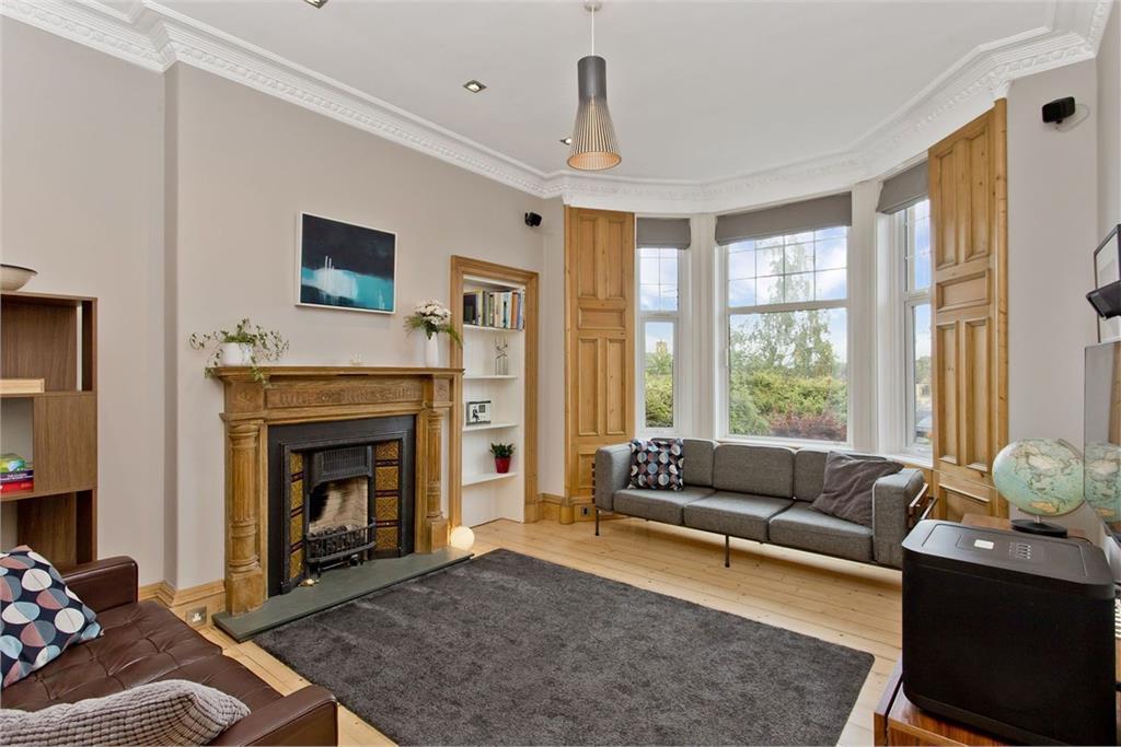 A large living room with bay windows and grey and wood furnishings.