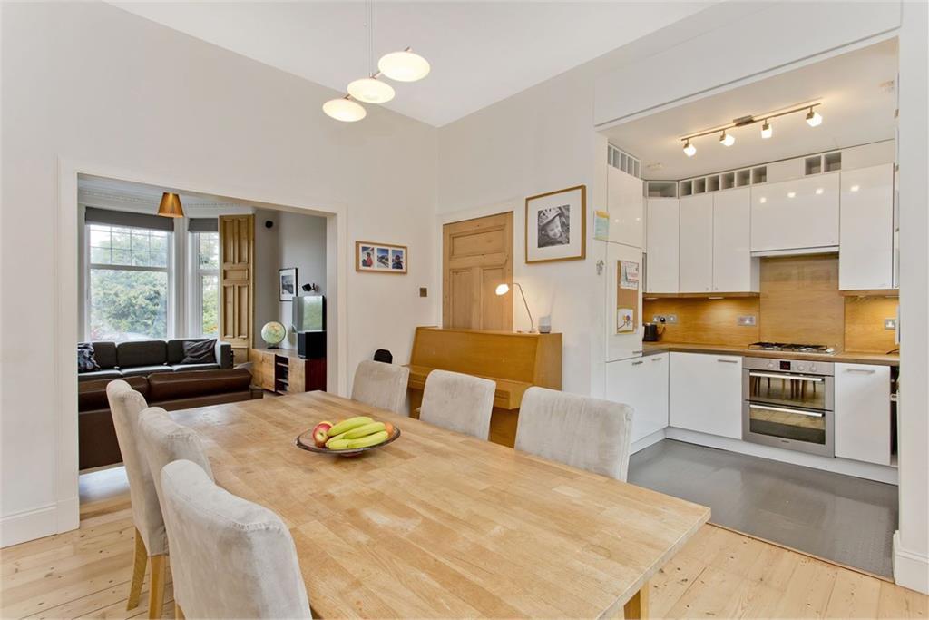 A large open-plan kitchen with white cabinets and white walls. The liivng room can be seen off in the background to the left.