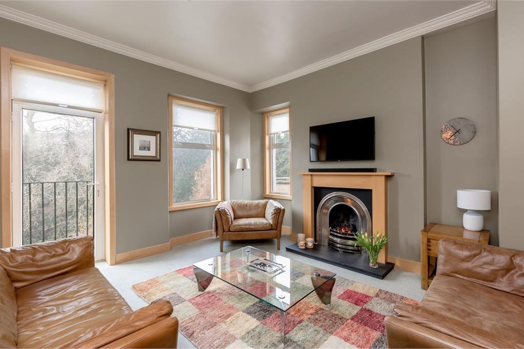 A large living room with light green walls, light wood frames, a fireplace and brown sofa and chairs.